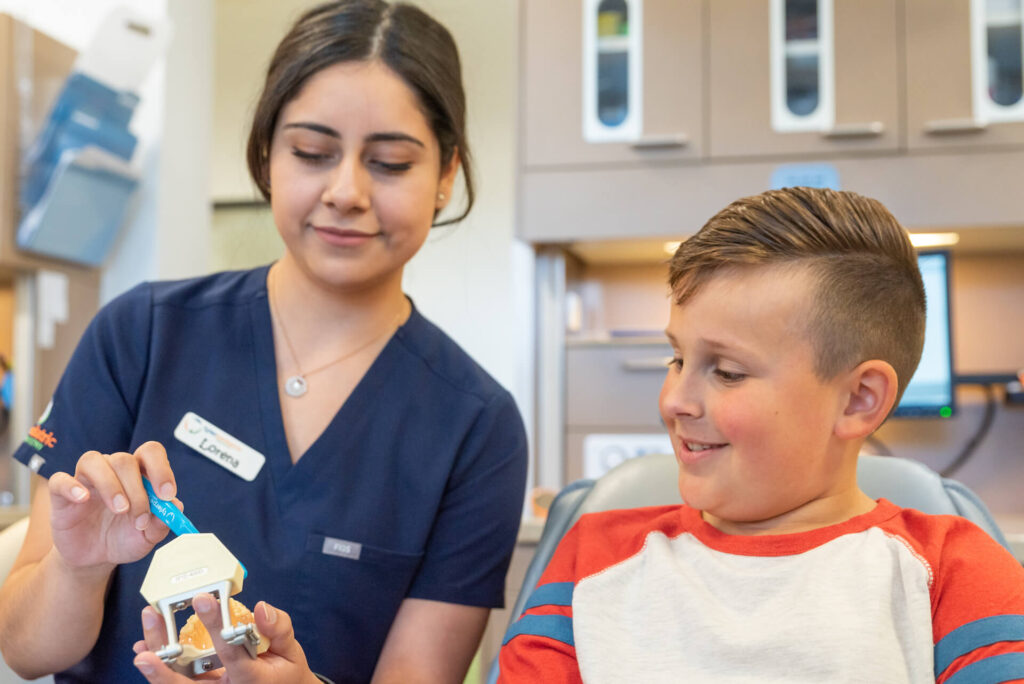 Tyler Pediatric Dentistry hygienist showing child how to brush teeth on model - Tyler, TX